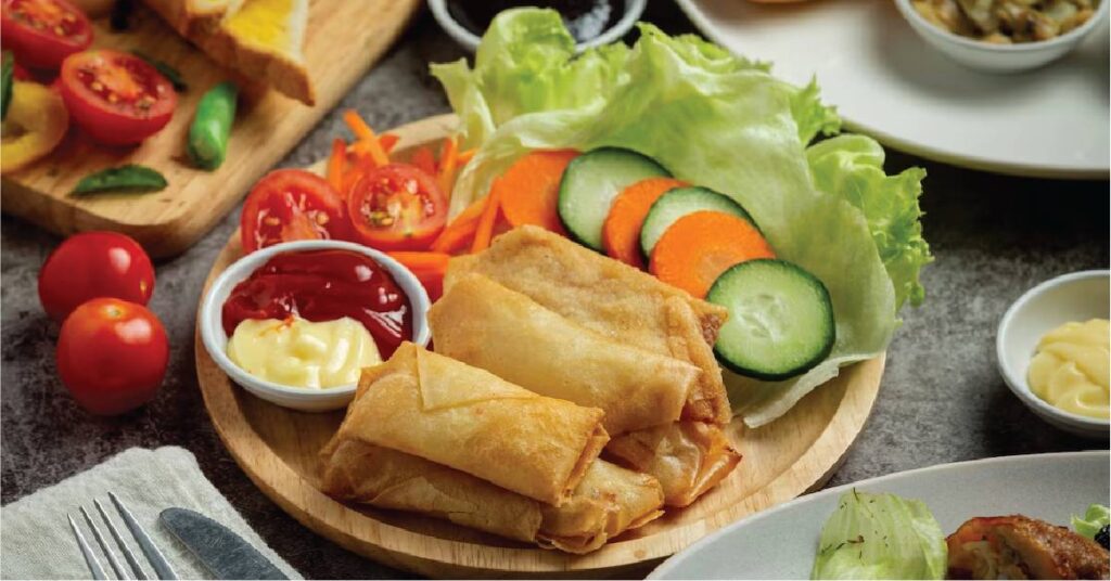 A plate of lumpiang shanghai with sauce and vegetables on the side